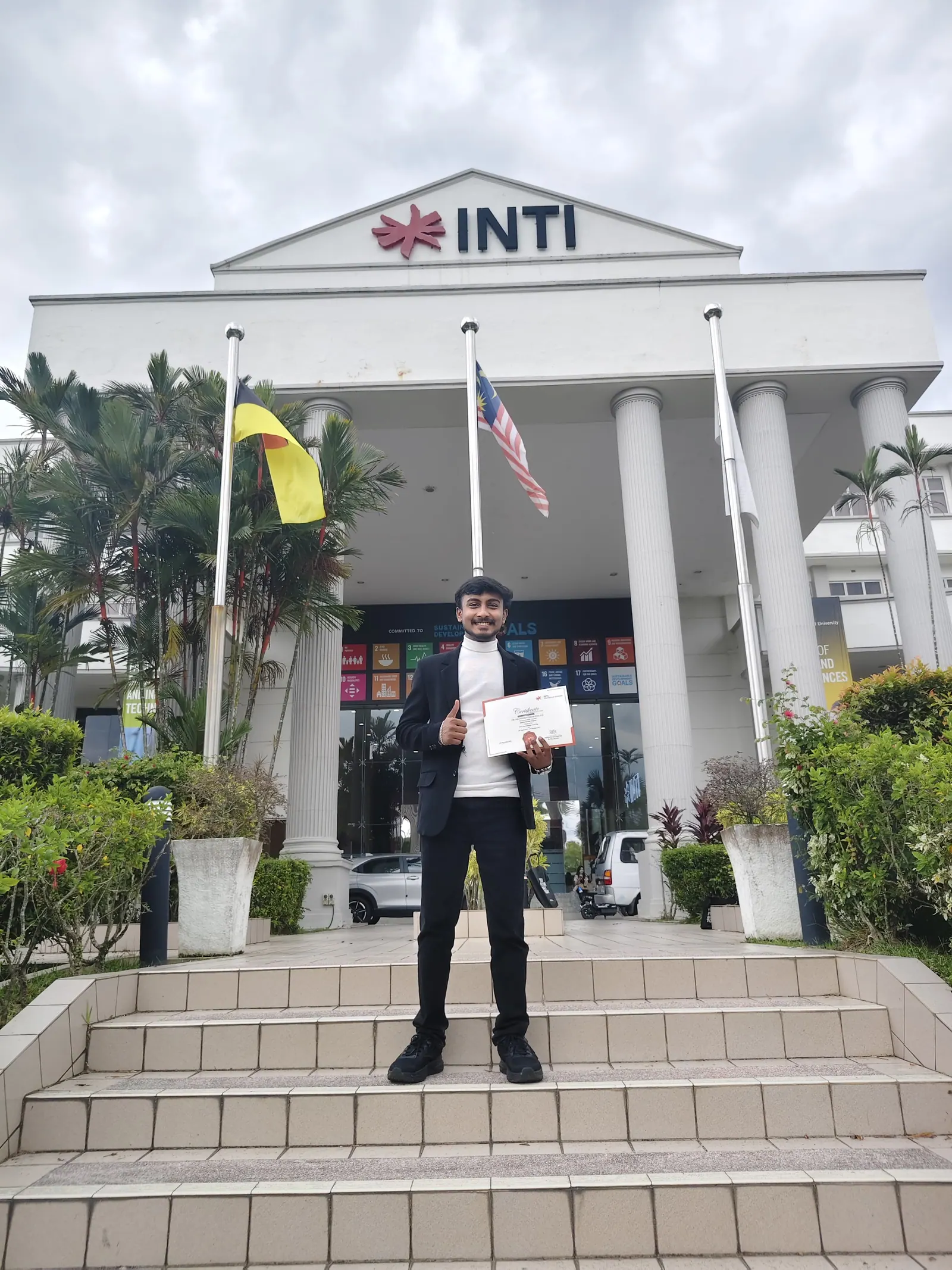 Prathamesh Halale holding a certificate in front of INTI International University in Malaysia